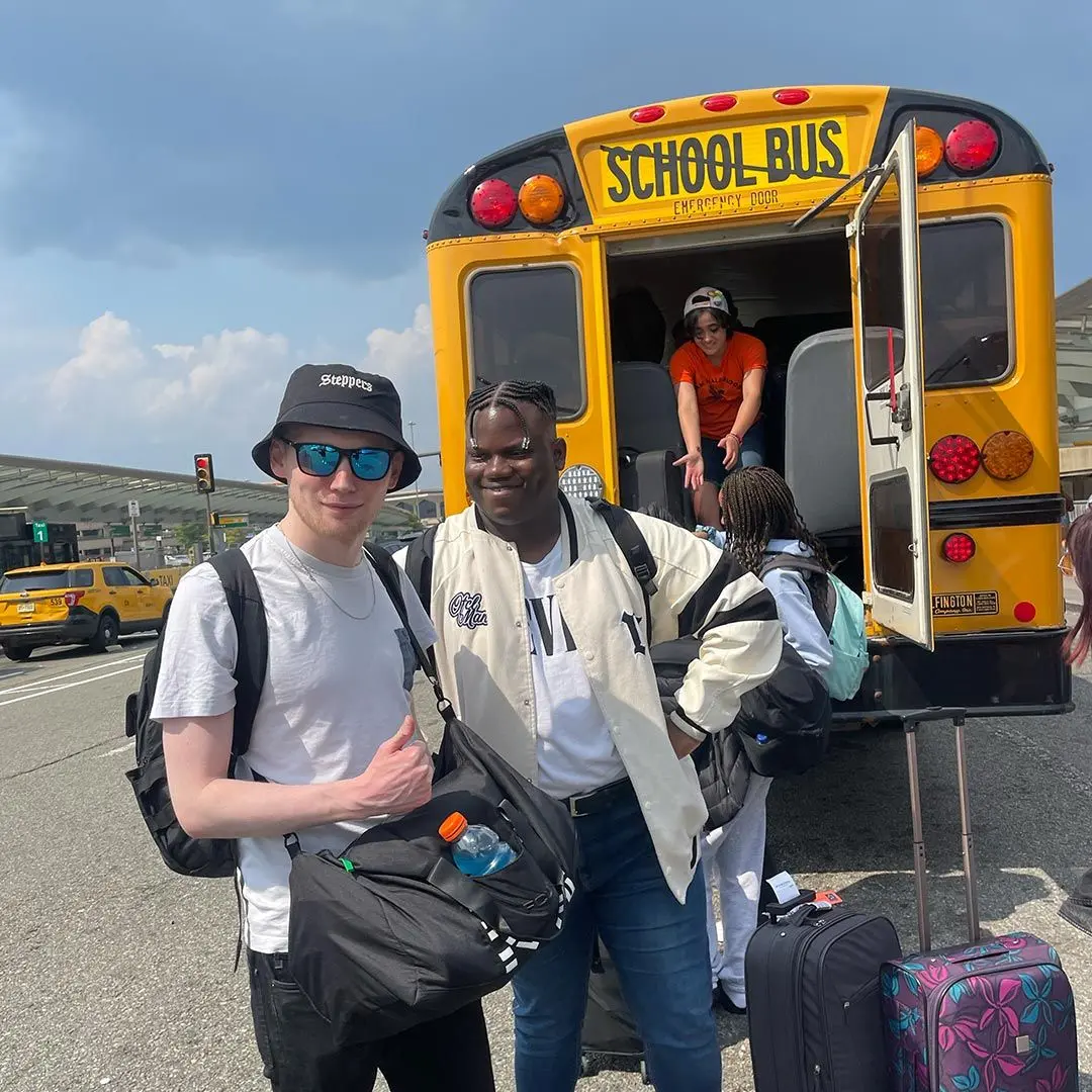 2 guys with bags behind school bus.
