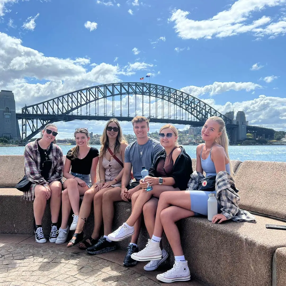 Group of 6 sits in front of bridge in Sydney on sunny day