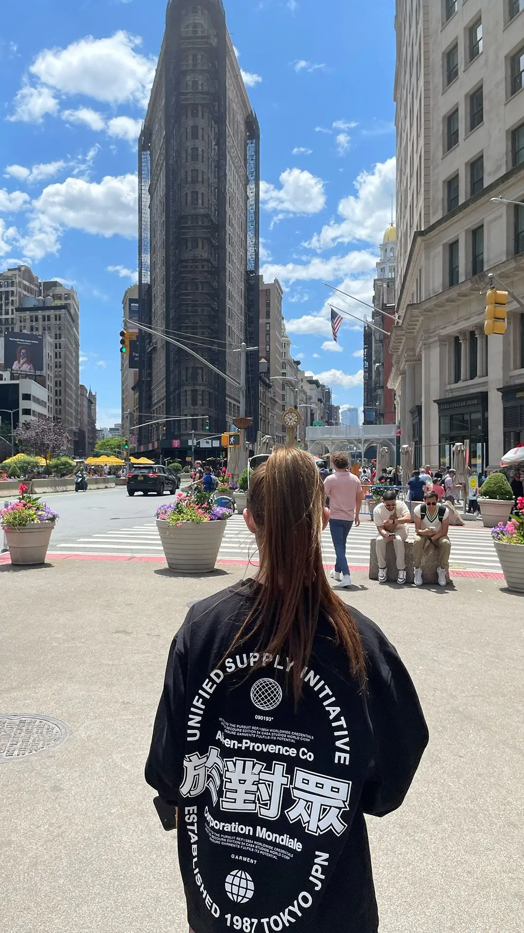 Girl facing away from camera in black jumper with white designs with New York Flat Iron building in the background.